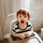 boy in black and white striped shirt sitting on white high chair